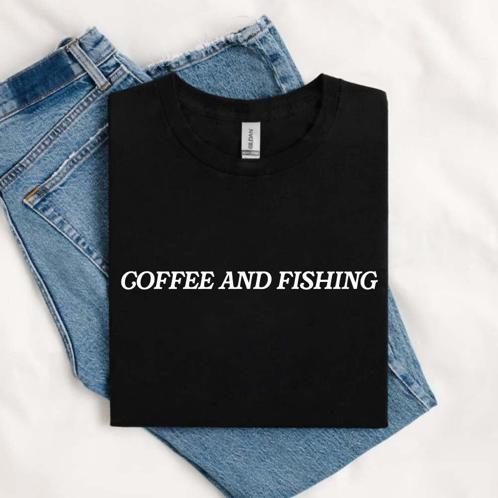 May include an image of a folded black unisex T-shirt with bold white “COFFEE AND FISHING” text, placed beside denim jeans, representing a casual fisherman and coffee lover’s outfit.