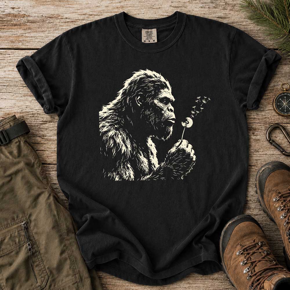 May include a Black Bigfoot blowing a dandelion graphic on a casual T-shirt for men and women with a funny Sasquatch blowing wishes design.
