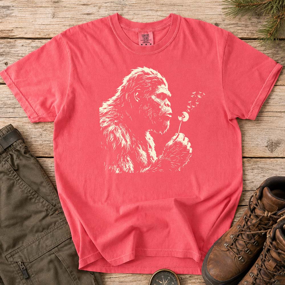 May include a Watermelon Bigfoot blowing a dandelion graphic on a casual T-shirt for men and women with a funny Sasquatch blowing wishes design.