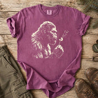 Thumbnail for May include a Berry Bigfoot blowing a dandelion graphic on a casual T-shirt for men and women with a funny Sasquatch blowing wishes design.