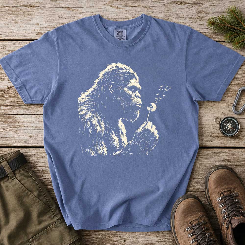 May include a Blue Jean Bigfoot blowing a dandelion graphic on a casual T-shirt for men and women with a funny Sasquatch blowing wishes design.