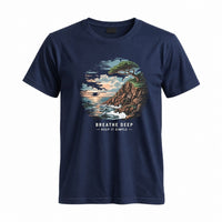 Thumbnail for May include a Navy Breathe Deep Keep It Simple T-Shirt featuring a scenic coastal landscape with ocean waves, rocky cliffs, a windswept tree, and an inspirational nature graphic.