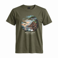 Thumbnail for May include a Military Green Breathe Deep Keep It Simple T-Shirt featuring a scenic coastal landscape with ocean waves, rocky cliffs, a windswept tree, and an inspirational nature graphic.
