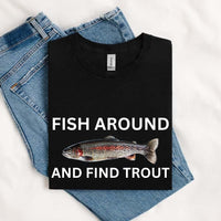 Thumbnail for May include a black unisex T-shirt with a colorful trout graphic and bold white text reading “Fish Around and Find Trout,” displayed folded with denim jeans