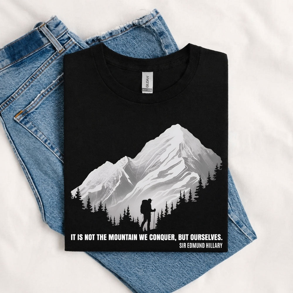 May include a Black It Is Not the Mountain We Conquer but Ourselves T-Shirt featuring an inspirational mountain quote graphic for hikers, climbers, campers, and mountain lovers.