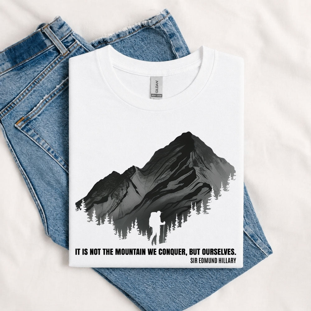 May include a White It Is Not the Mountain We Conquer but Ourselves T-Shirt featuring an inspirational mountain quote graphic for hikers, climbers, campers, and mountain lovers.
