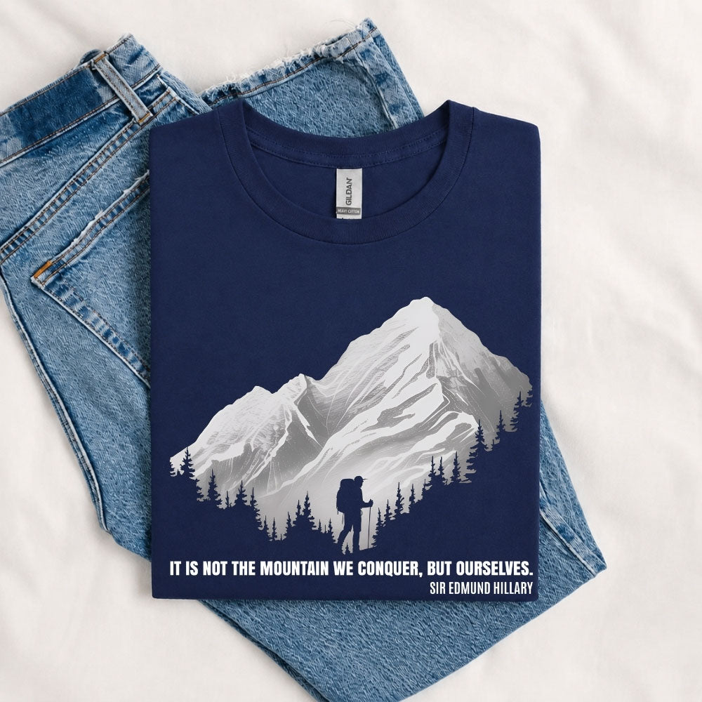 May include a Navy It Is Not the Mountain We Conquer but Ourselves T-Shirt featuring an inspirational mountain quote graphic for hikers, climbers, campers, and mountain lovers.