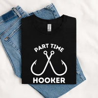 Thumbnail for May include an image of a folded black unisex T-shirt with two crossed fishing hooks and the text “PART TIME HOOKER” printed in bold white lettering, styled next to denim jeans for a casual fishing-inspired outfit.