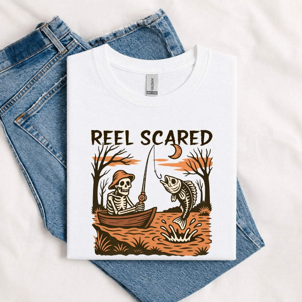 May include a White person wearing the Reel Scared Halloween T-Shirt featuring a funny fishing-inspired Halloween graphic for spooky season celebrations.